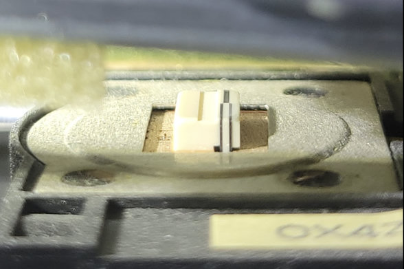 A close in zoom of "Head 0" from a 5.25" floppy drive, showing it as a biege plastic gubbin in the middle of a cutout in a metal plate.