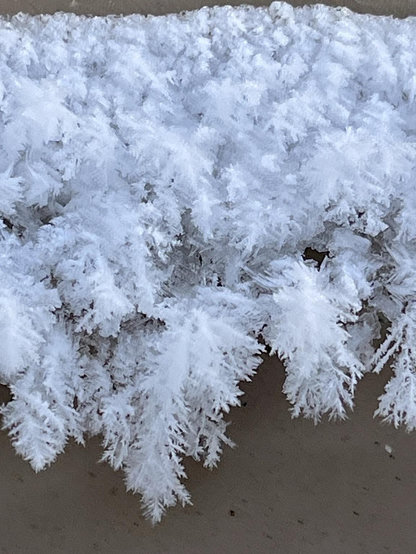 A close-up view of frost covering a surface, showcasing intricate, crystalline formations that resemble delicate, frozen foliage.