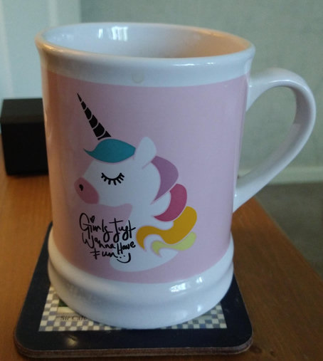 Tankard shape mug of tea on a bedside cabinet, with a pink background and a unicorn with a rainbow mane
