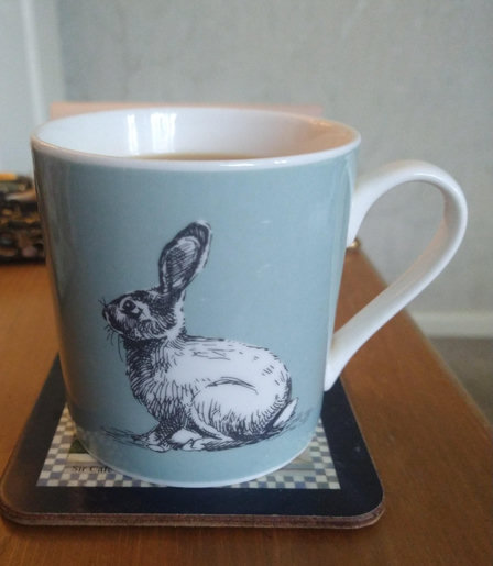 Pale blue mug of tea on a bedside cabinet with a picture of a young leveret in the centre