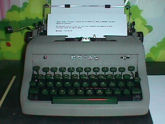 A 1954 Royal Quiet De Luxe typewriter with a backed page inserted and paper lock lifted out of the way to show the typewriting. According to a 1955 ad, this is probably the Dove Gray color: a medium drab gray shell and deep sea green key caps. Photo taken with a 1998 Sony Mavica MVC-FD51 camera with flash on.