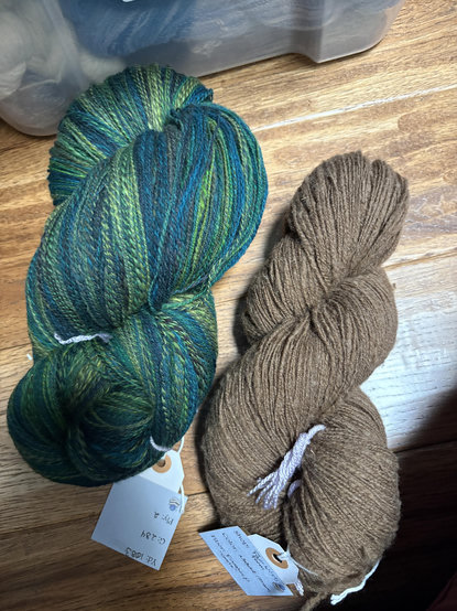 Two skeins of handspun yarn. One is several shades of green, the other is brown. 
