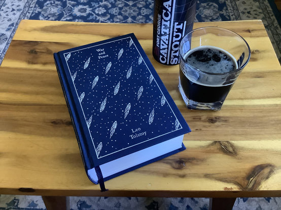 The book, War and Peace, by Leo Tolstoy, next to a glass of imperial stout.