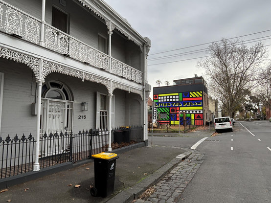 A building with elaborate cast-iron decoration stands in front of a colourful mural.
