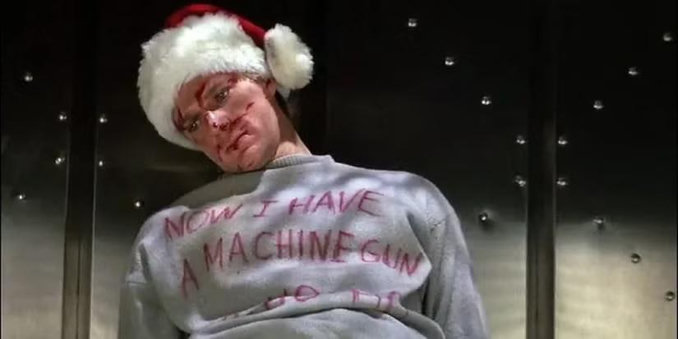 Dead thug from Die Hard wearing Santa hat and sweatshirt with the text "Now I have a machine gun Ho Ho Ho"