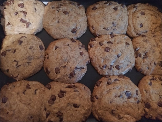Foto de 12 cookies com gotas de chocolate em uma assadeira retangular. Eles estão grudados um no outro pois expandiram enquanto assavam